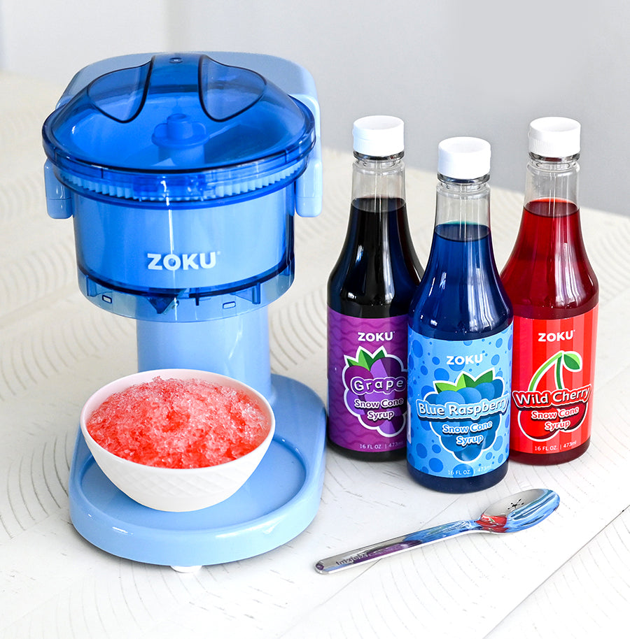 The ZOKU Snow Cone Maker beside bottles of ZOKU Grape, Blue Raspberry, and Wild Cherry Snow Cone Syrups.